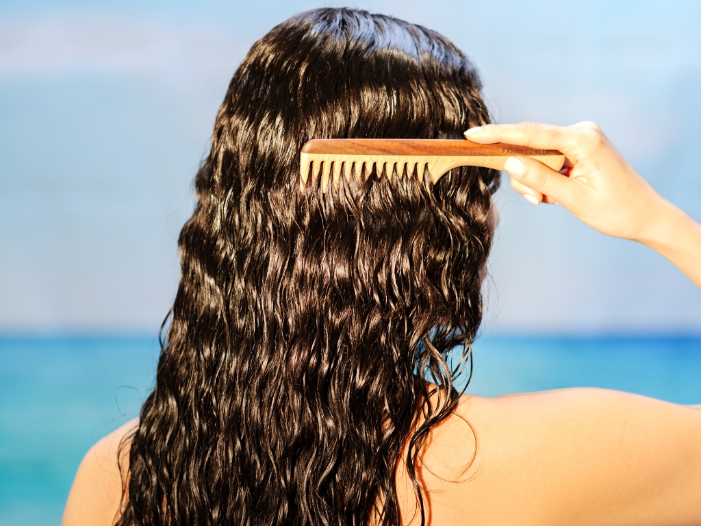 11 Model with hydrated, healthy wavy curly hair using a wooden comb for low porosity summer hair care