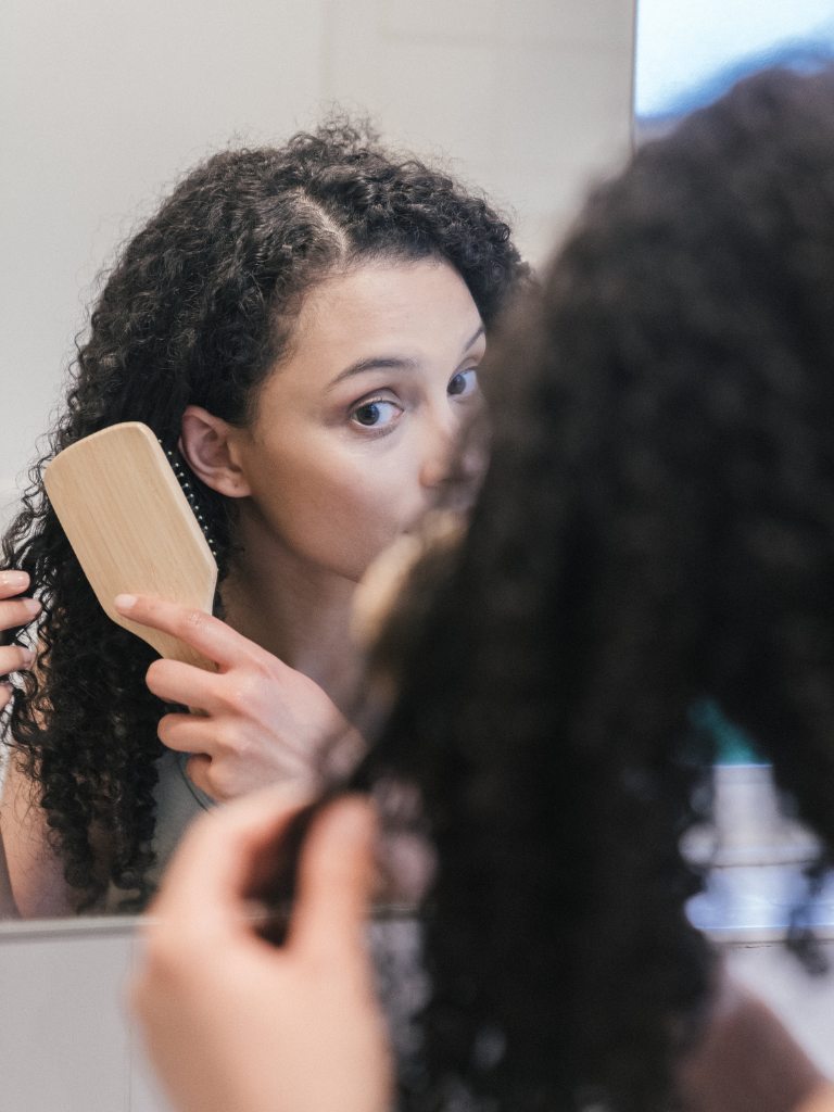 Untitled design Curly-haired model brushing hair and checking for dryness, highlighting challenges of low porosity curls
