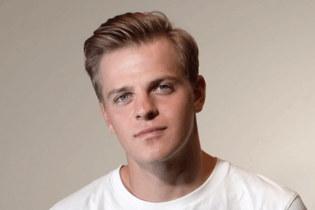 Man with styled hair wearing a white shirt, showcasing a sleek, polished men’s blowout with a side part and natural volume.